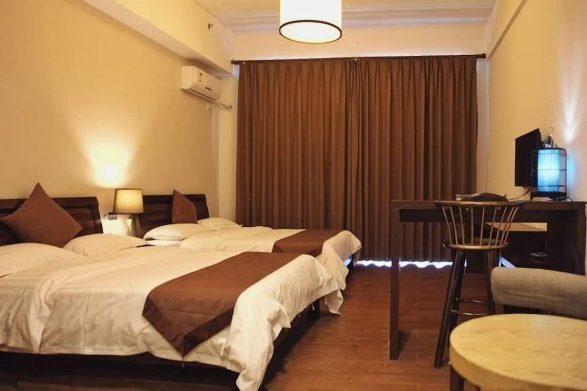A hotel room with two beds, a desk, a chair, a TV, and a lamp.
