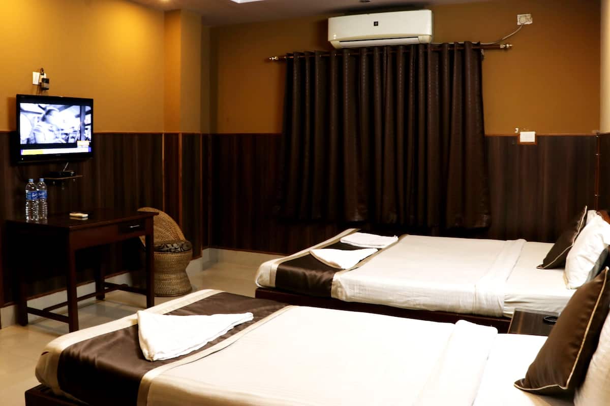 A hotel room with two beds, a desk with a television, and an air conditioning unit.
