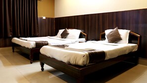 Two single beds with wooden frames and white bedding, in a room with dark wooden walls and a tiled floor. - Om Shree Residency (Guwahati)
