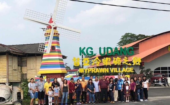 A group of people in front of a colorful windmill and a sign for KG UDAng MyPrawn Village. - MyPrawn Village (Tanjung Tualang)