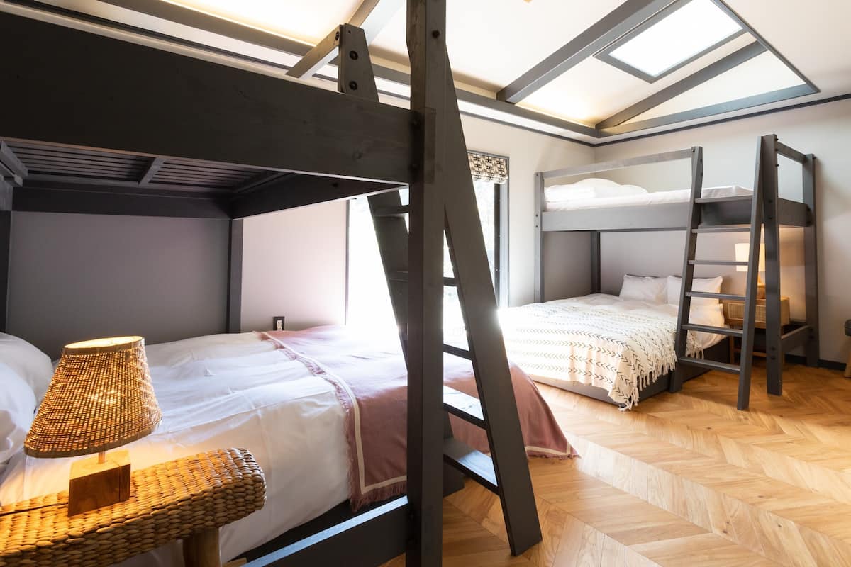 A room with bunk beds, a ladder, a small table with books, and a lamp.