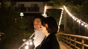 A couple standing on a bridge with string lights in the background. - Riverside Lodge (Uwajima)