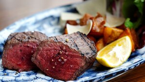 Un plato de carne con rodaja de limón y patatas asadas.