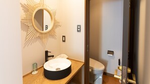 Un baño moderno con un lavabo redondo, un espejo con marco en forma de sol, un inodoro y una zona de ducha.