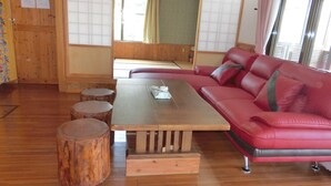 Ein Zimmer mit Holzboden, einem roten Sofa, einem Holztisch und einem Fenster mit Blick auf Grünflächen.