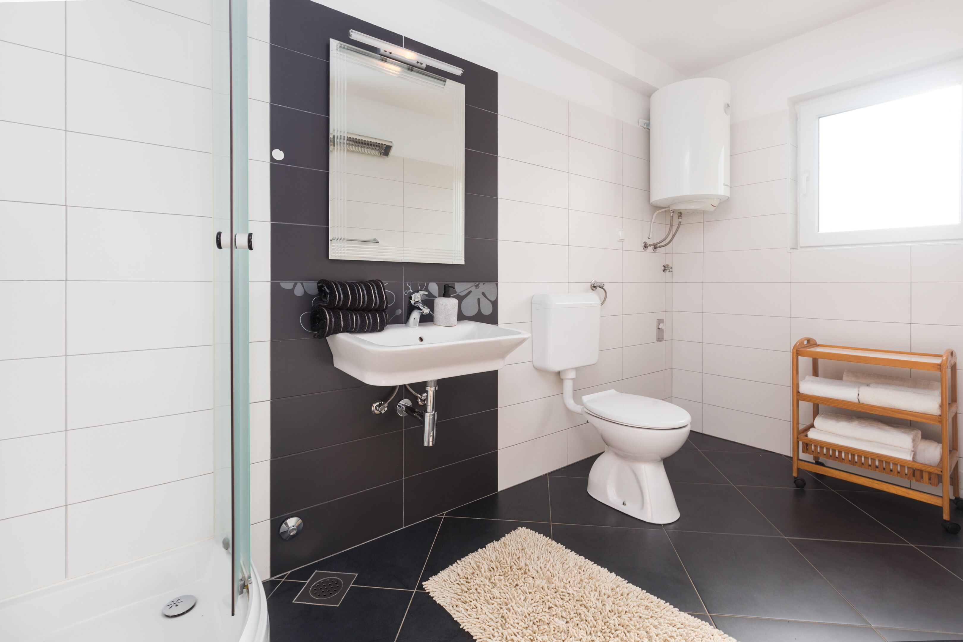 A modern bathroom with a glass shower enclosure, a white sink, a toilet, and a wooden towel rack.