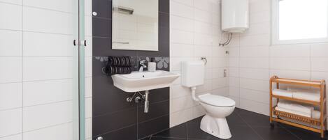 A modern bathroom with a glass shower enclosure, a white sink, a toilet, and a wooden towel rack.