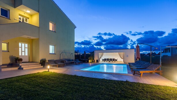 Un bâtiment moderne à deux étages doté d’une piscine, d’un espace extérieur aménagé et d’une pelouse bien entretenue.