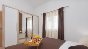 Une chambre d’hôtel avec un lit, une table de chevet en bois sur laquelle se trouve un plateau de petit-déjeuner, un miroir et une fenêtre avec des rideaux.