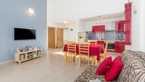 Un salon moderne doté d’un téléviseur à écran plat, d’un meuble de rangement en bois et d’un canapé à motifs avec des coussins rouges.