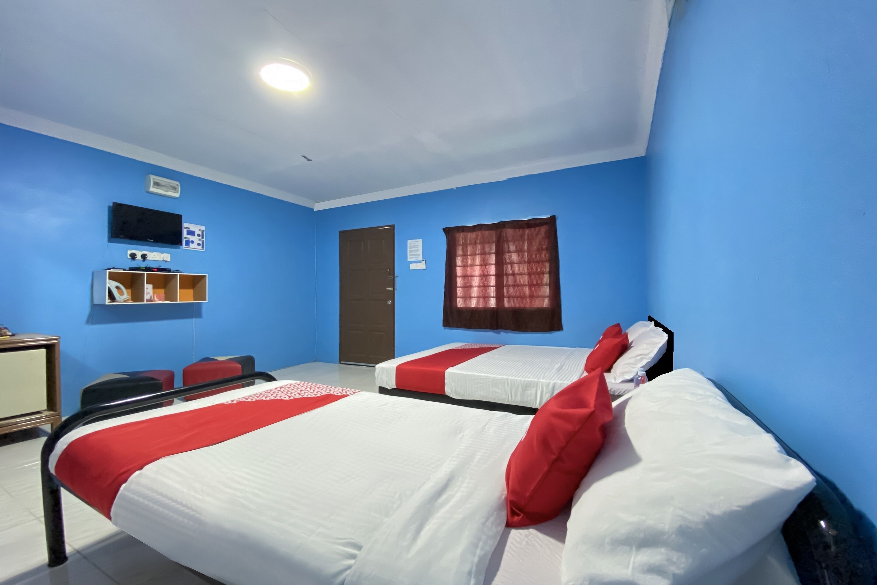 A hotel room with two beds, a desk, a chair, a TV, and a window with curtains.