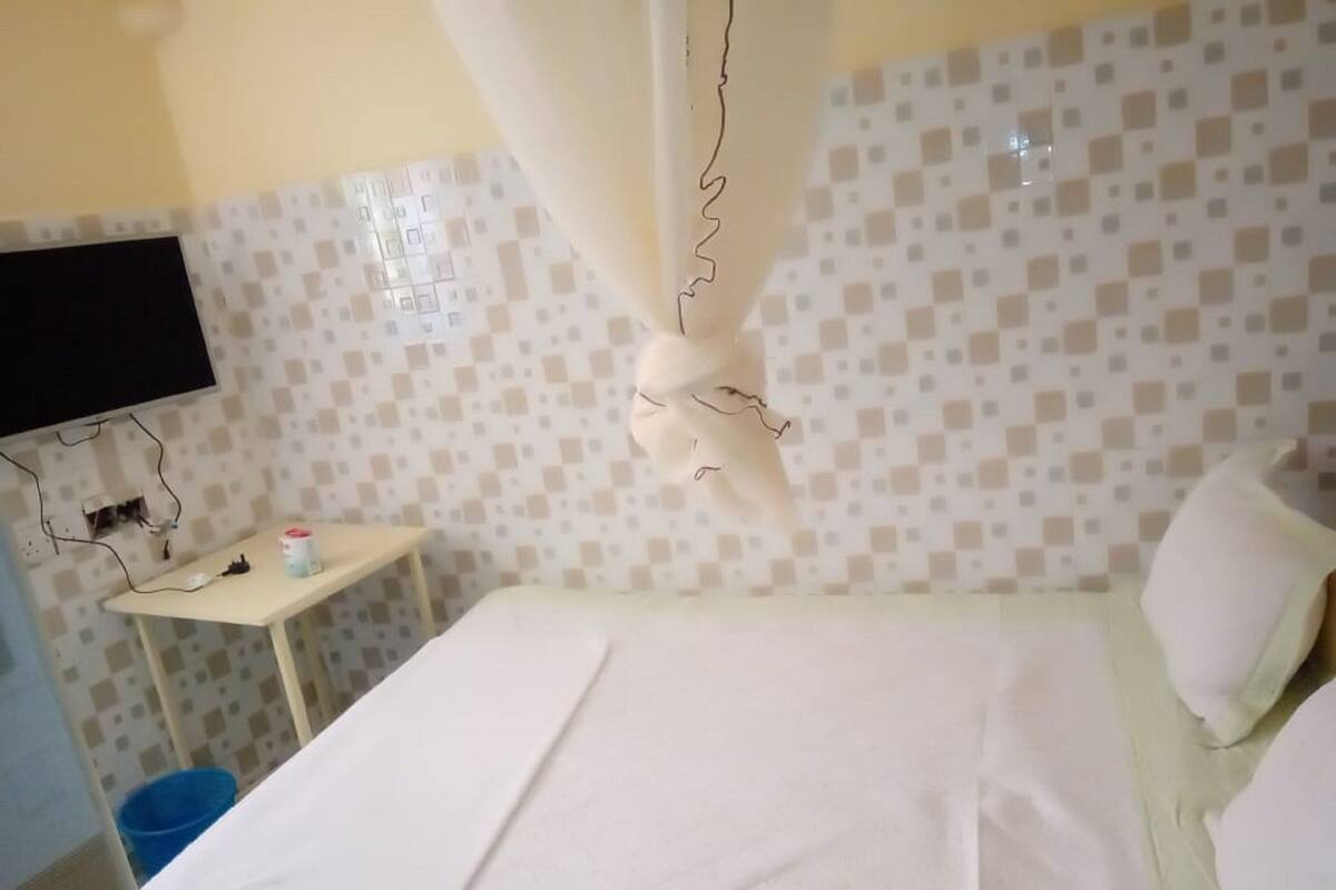 A hotel room with a bed, a television mounted on the wall, and a small table with a cup.