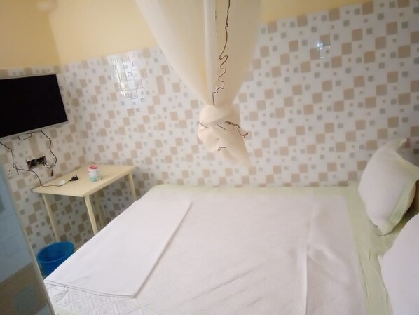 A hotel room with a bed, a television mounted on the wall, and a small table with a cup.