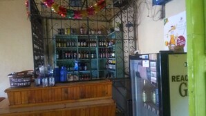 Una zona de bar con estantes llenos de botellas, una barra con vasos y un refrigerador.
