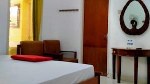 A hotel room with a bed, a chair, a table with a mirror, and an air conditioning unit on the wall. - Prayogolama Guest House (Yogyakarta)