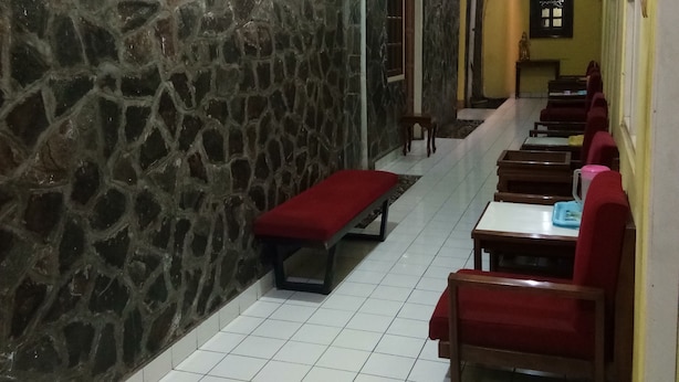A restaurant with stone walls, tiled floors, and red benches. - Prayogolama Guest House (Yogyakarta)