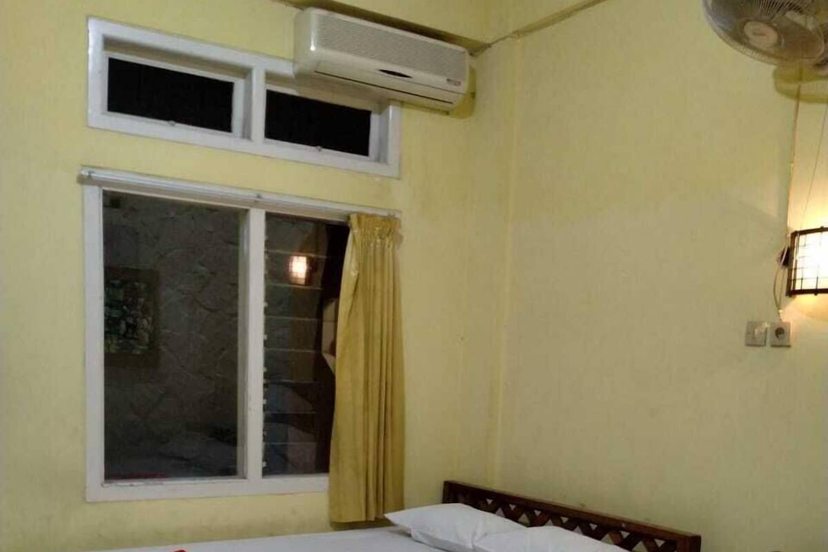 A room with two beds, a window with curtains, an air conditioning unit, and a wall-mounted fan.