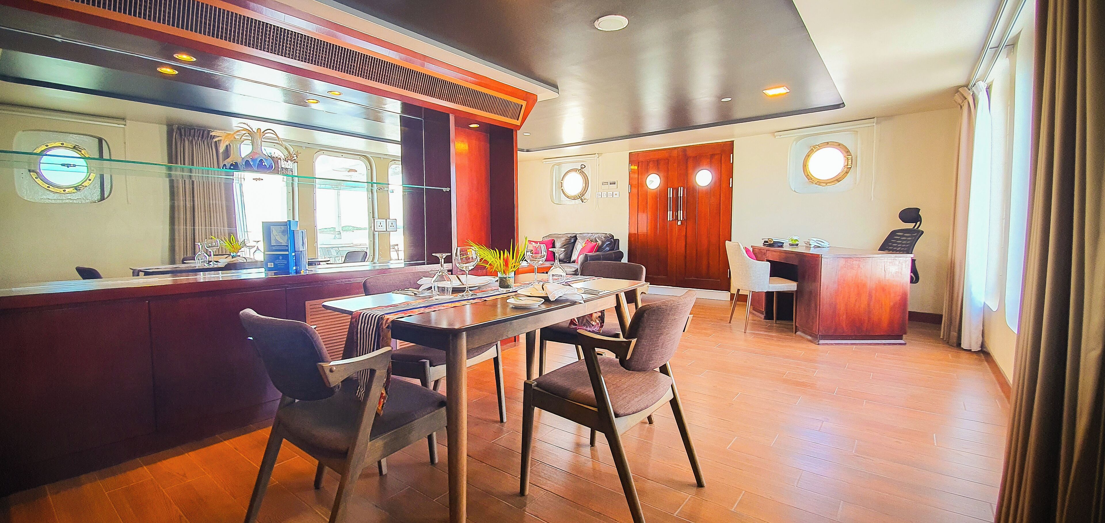 Comedor con mesa de madera, sillas y barra. Se observan dos puertas al fondo, una con un espejo y la otra con un teléfono.