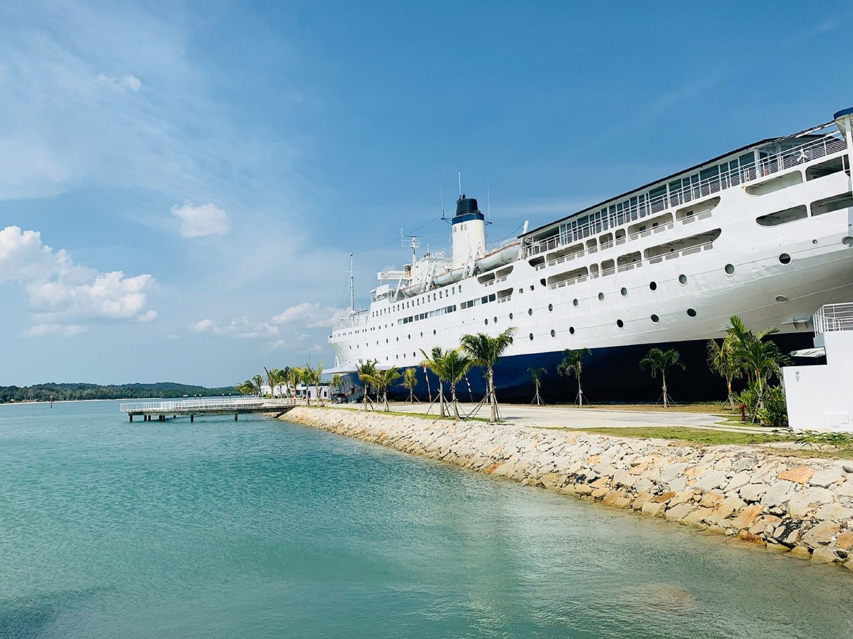 Un grand navire de croisière  était amarré à un quai bordé d’un mur de pierres et, au premier plan, on pouvait voir des palmiers.