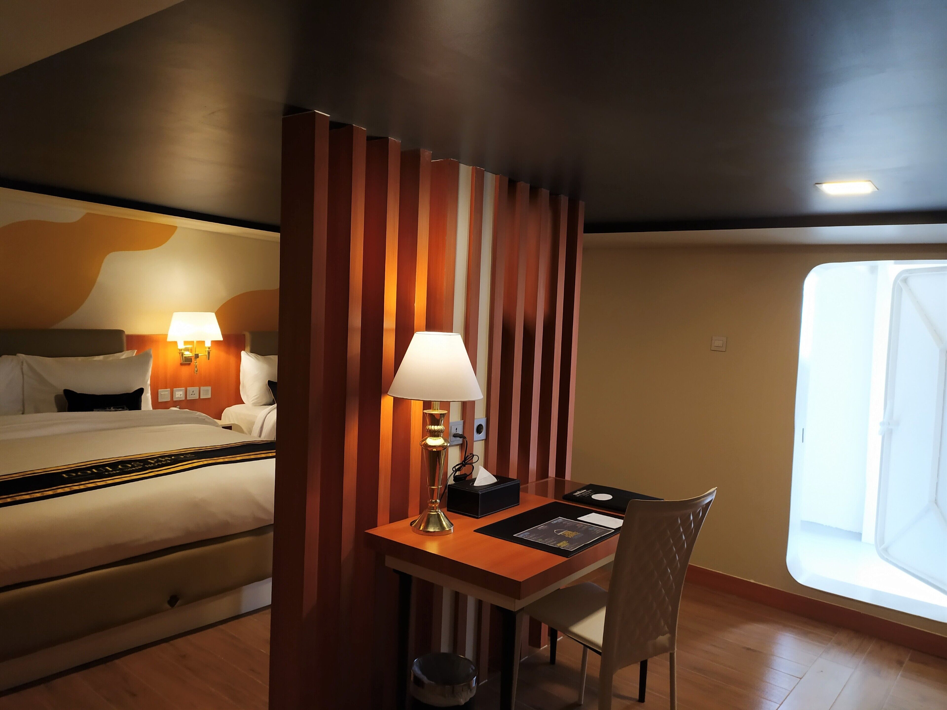 A hotel room with a bed, bedside lamps, a desk with a lamp, a chair, and a window.