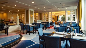A hotel restaurant with blue upholstered chairs, a marble bar area, and a statue in the background. - Pantower International Hotel (Jiangmen)