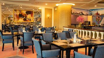 A restaurant with blue upholstered chairs, black tables, and a bar area with a decorative vase.