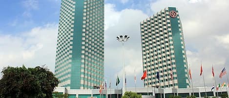 Two tall, modern buildings with a checkered facade, surrounded by flags and greenery.