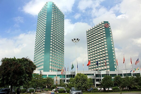 Two tall, modern buildings with a checkered facade, surrounded by flags and greenery. - Pantower International Hotel (Jiangmen)