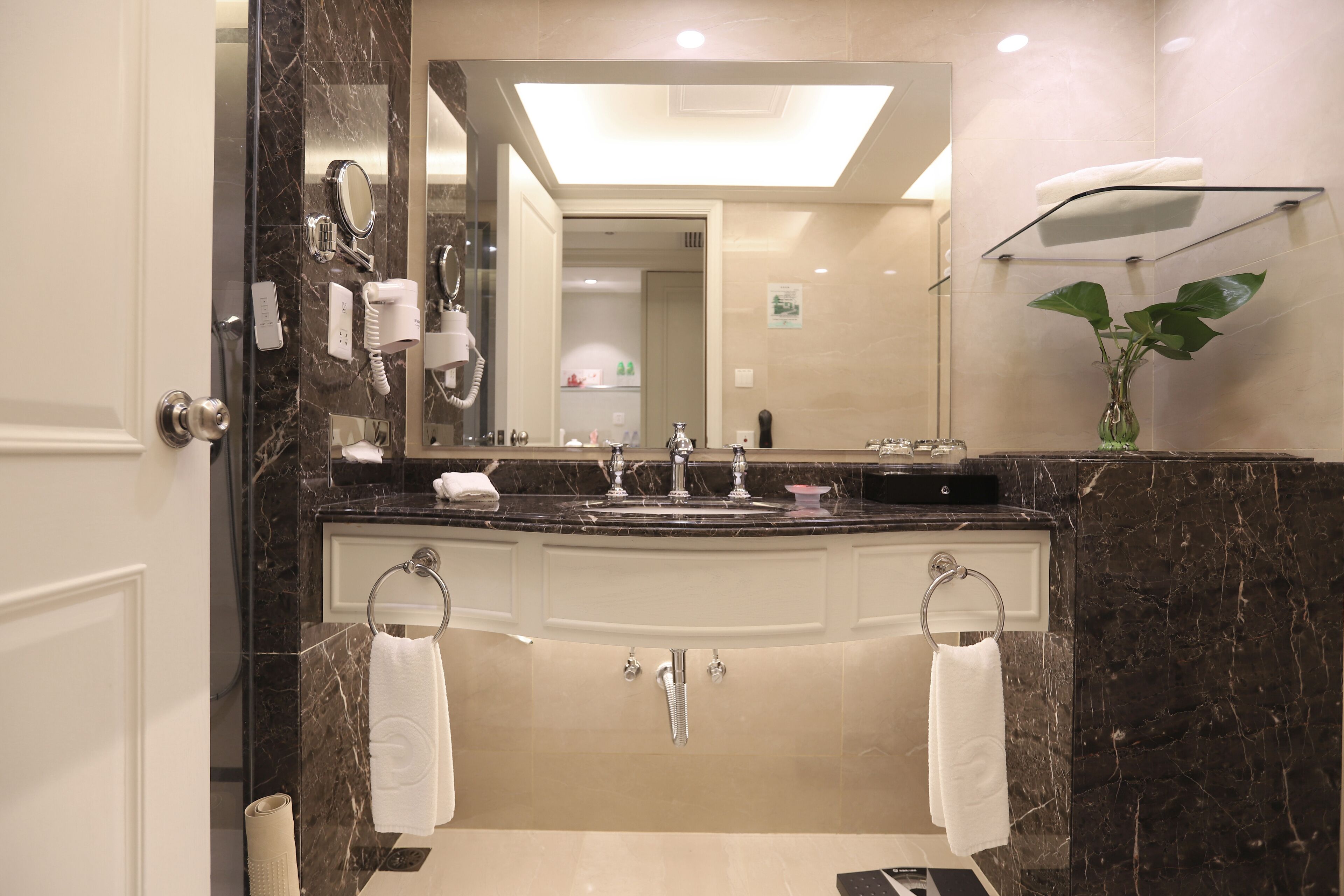 Un baño moderno con un espejo grande, dos lavamanos, un perchero para toallas y una planta.