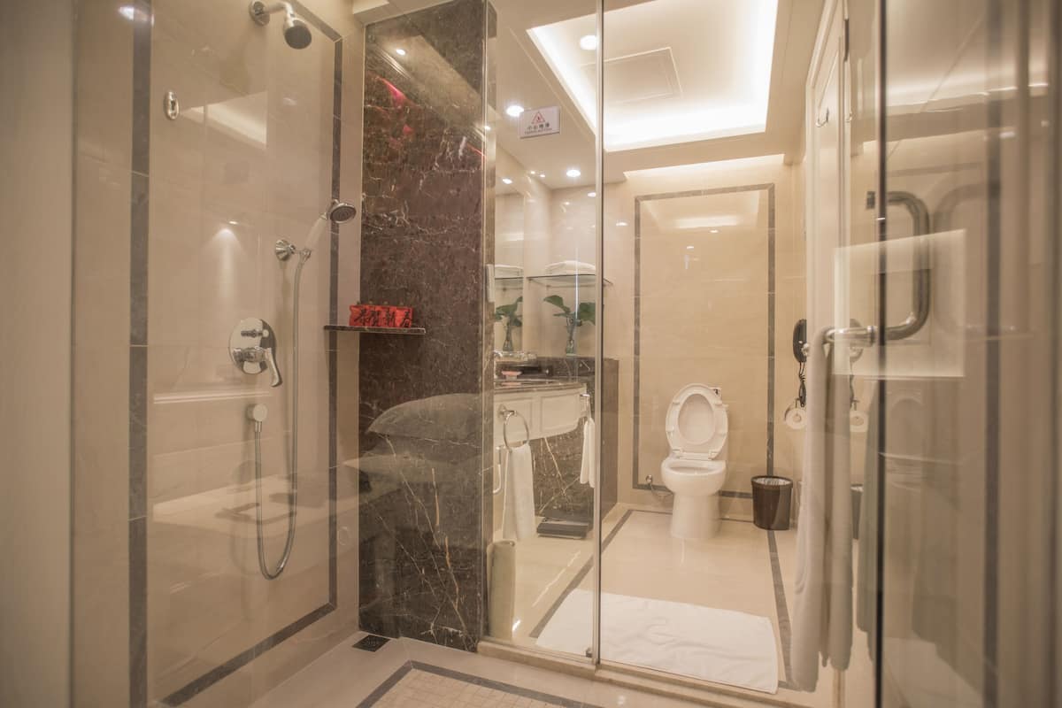 A modern bathroom with a glass-enclosed shower, a marble-tiled wall, a white toilet, and a sink with a mirror above it.