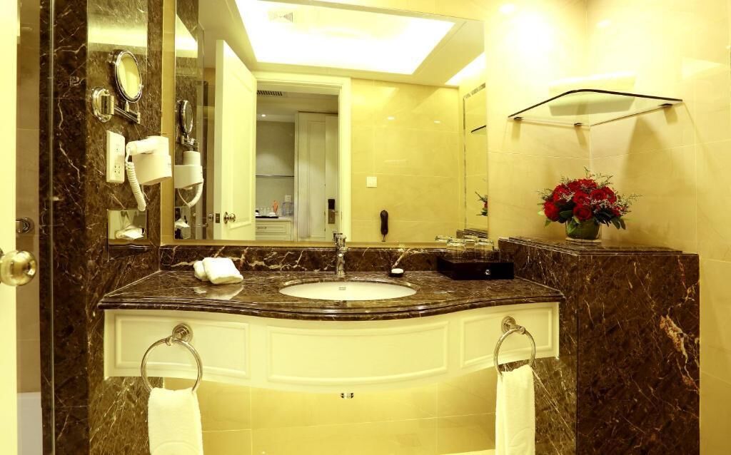 A bathroom with a marble sink, a mirror, a towel rack, a telephone, and a vase with flowers.
