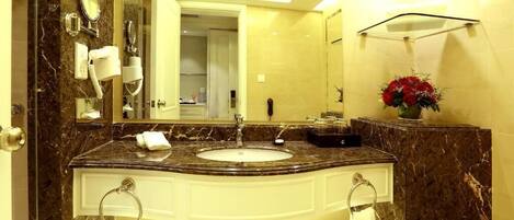 A bathroom with a marble sink, a mirror, a towel rack, a telephone, and a vase with flowers.