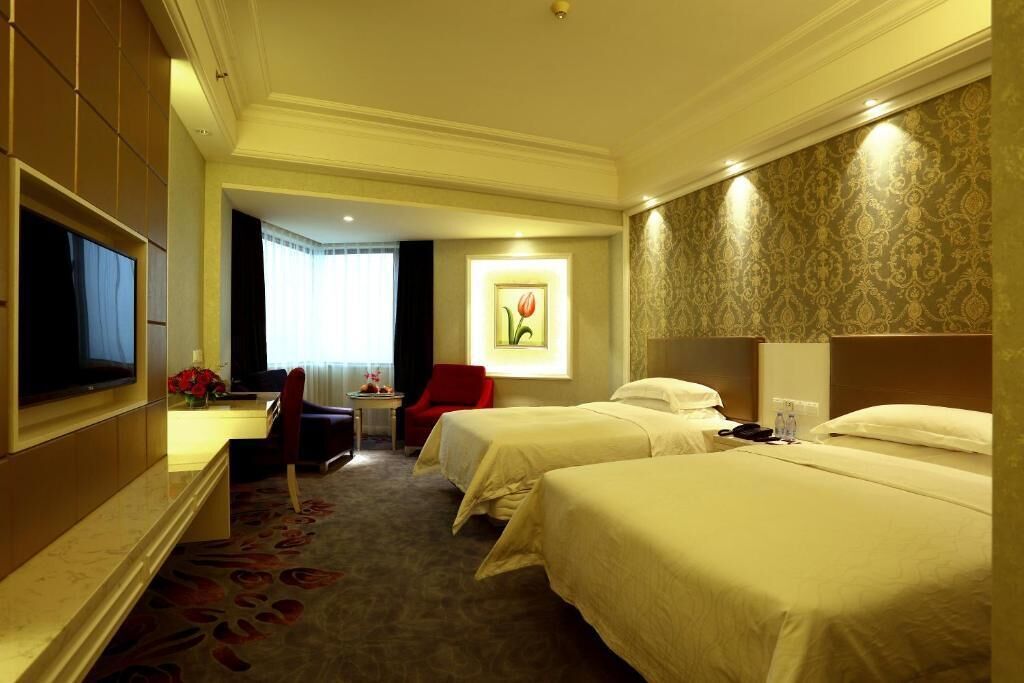 A hotel room with two beds, a desk, a TV, and a red chair.