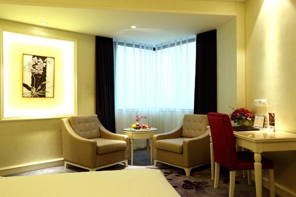 A hotel room with two armchairs, a small round table with fruit and flowers, a desk with a chair, and a bed.