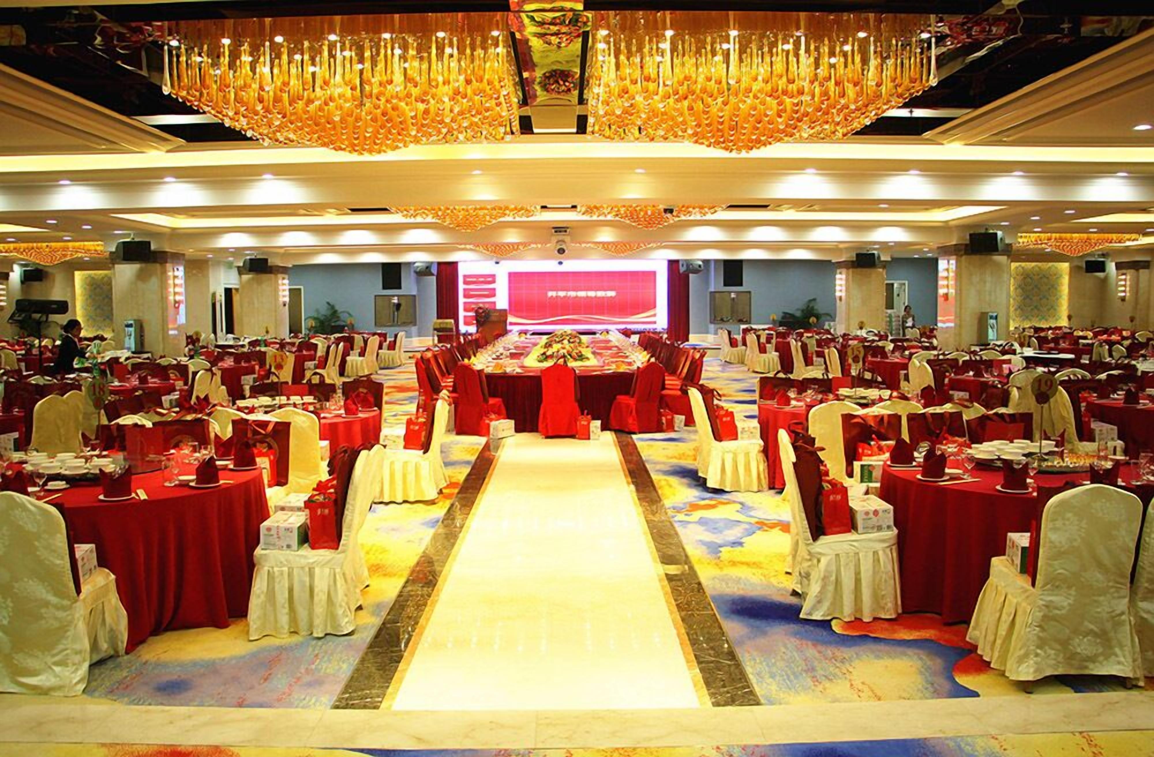 Un salón de banquetes con mesas dispuestas en filas, manteles rojos y sillas blancas.