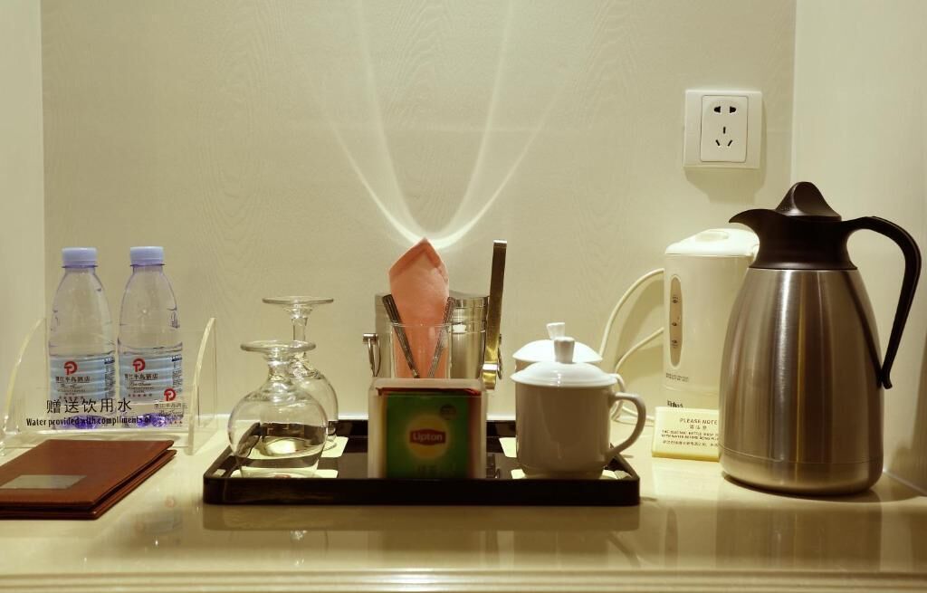 A kitchen counter with a tray holding a water bottle, a glass, a tea kettle, a coffee pot, and a box of Lipton tea.