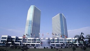 A modern building with two tall towers, a central fountain, and multiple flags. - Pantower International Hotel (Jiangmen)