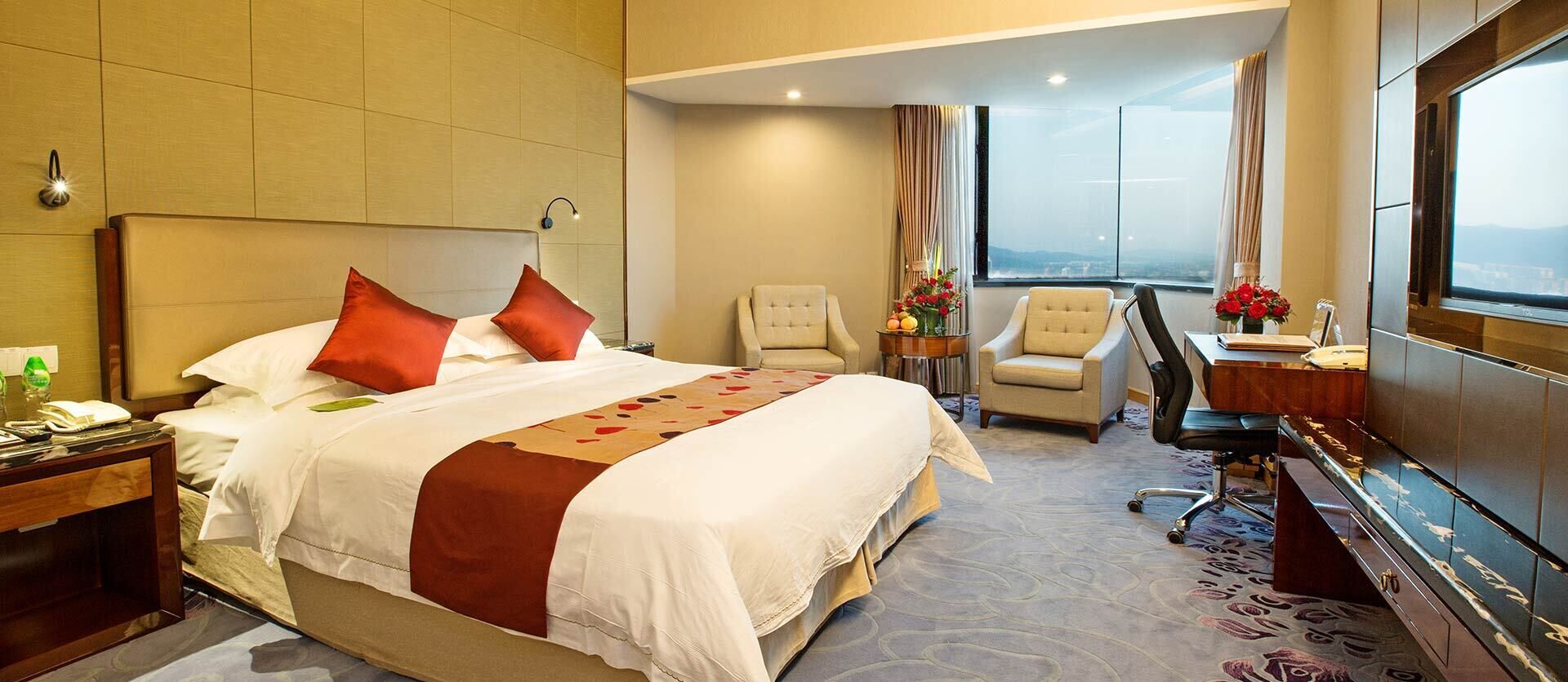 Habitación de hotel con cama, dos sillas, escritorio y un ventanal con vistas a la ciudad.