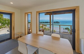 Une pièce moderne dotée d’une grande table et de chaises, de larges fenêtres offrant une vue sur la mer et une petite île.
