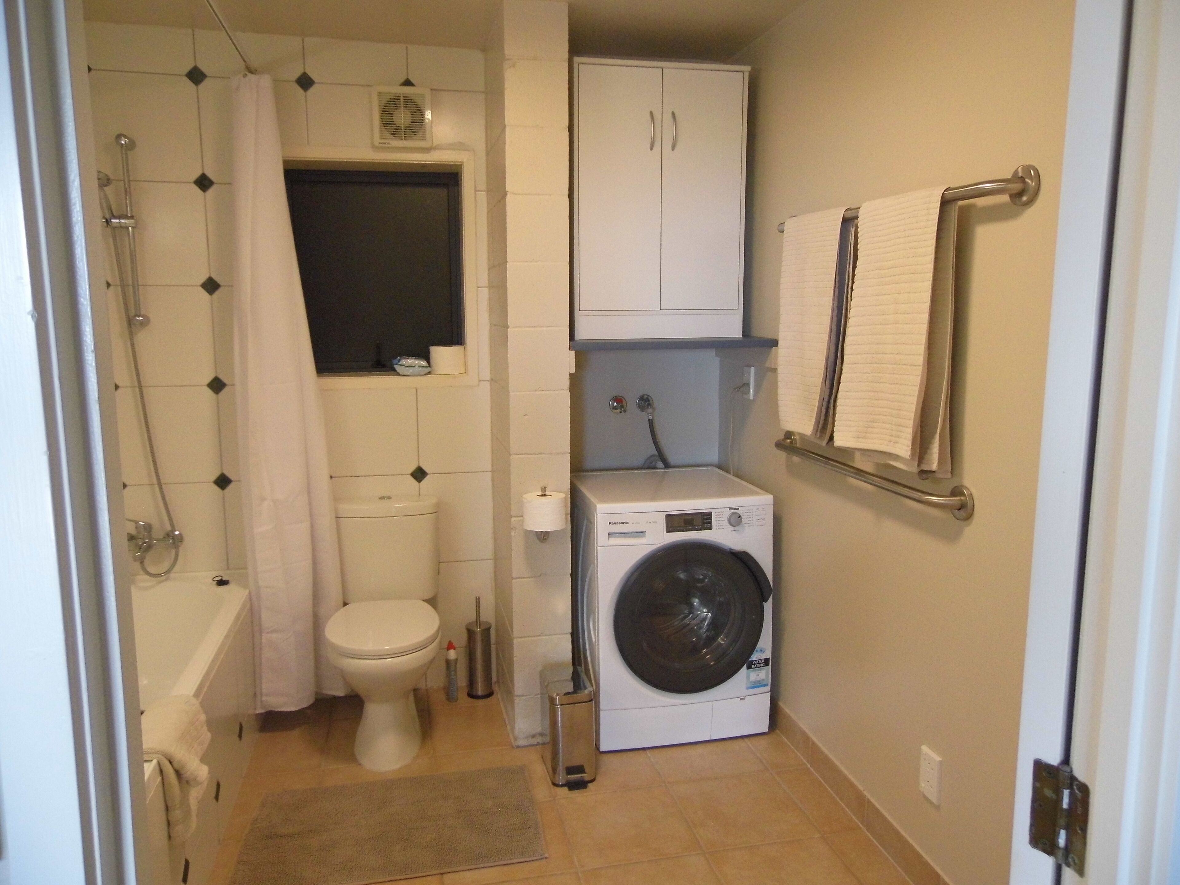 Une petite salle de bain comprenant des toilettes, une douche et un lave-linge.