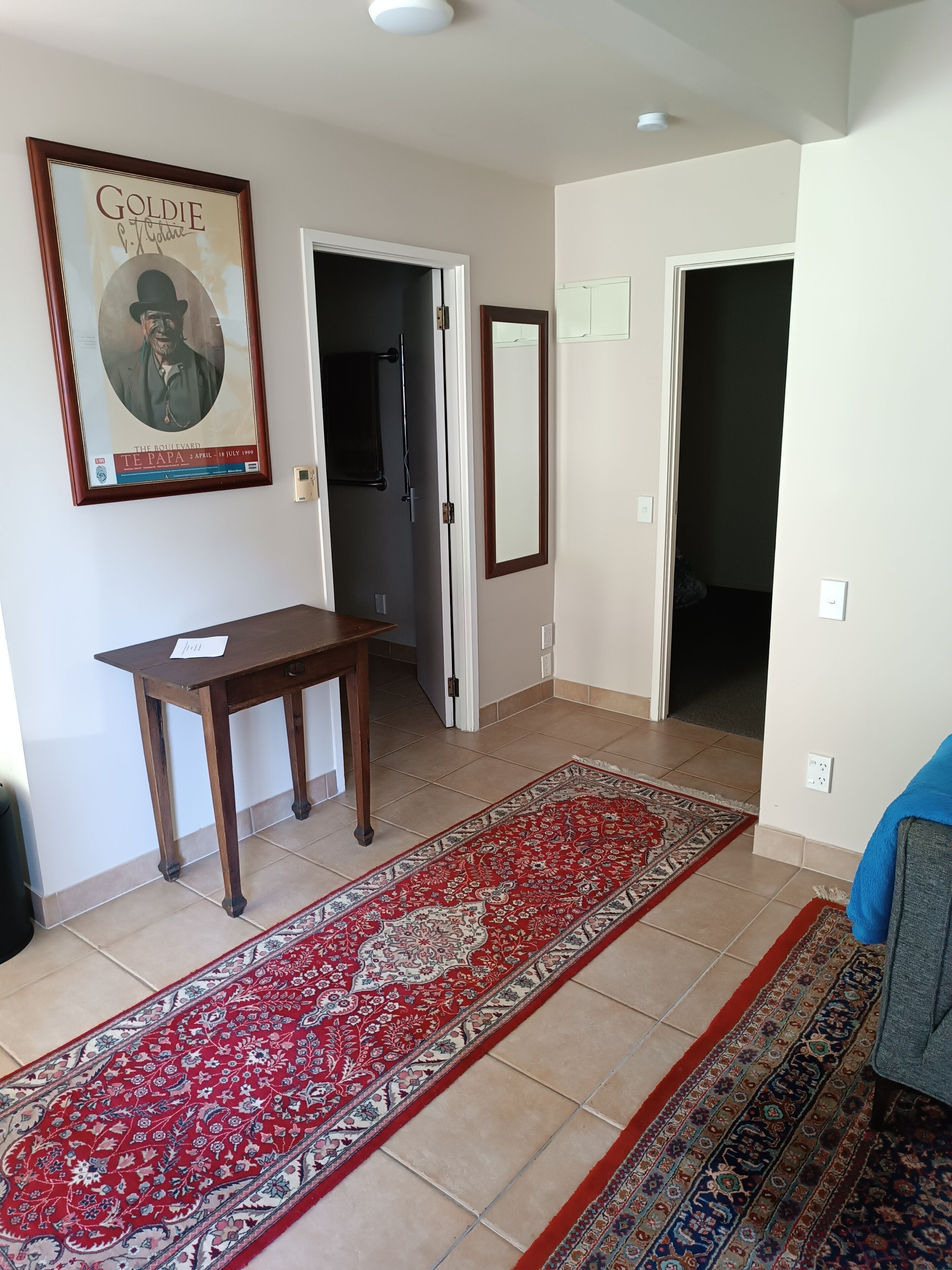 Un pasillo con un cartel enmarcado, una mesa de madera, un tapete estampado y un sofá azul.