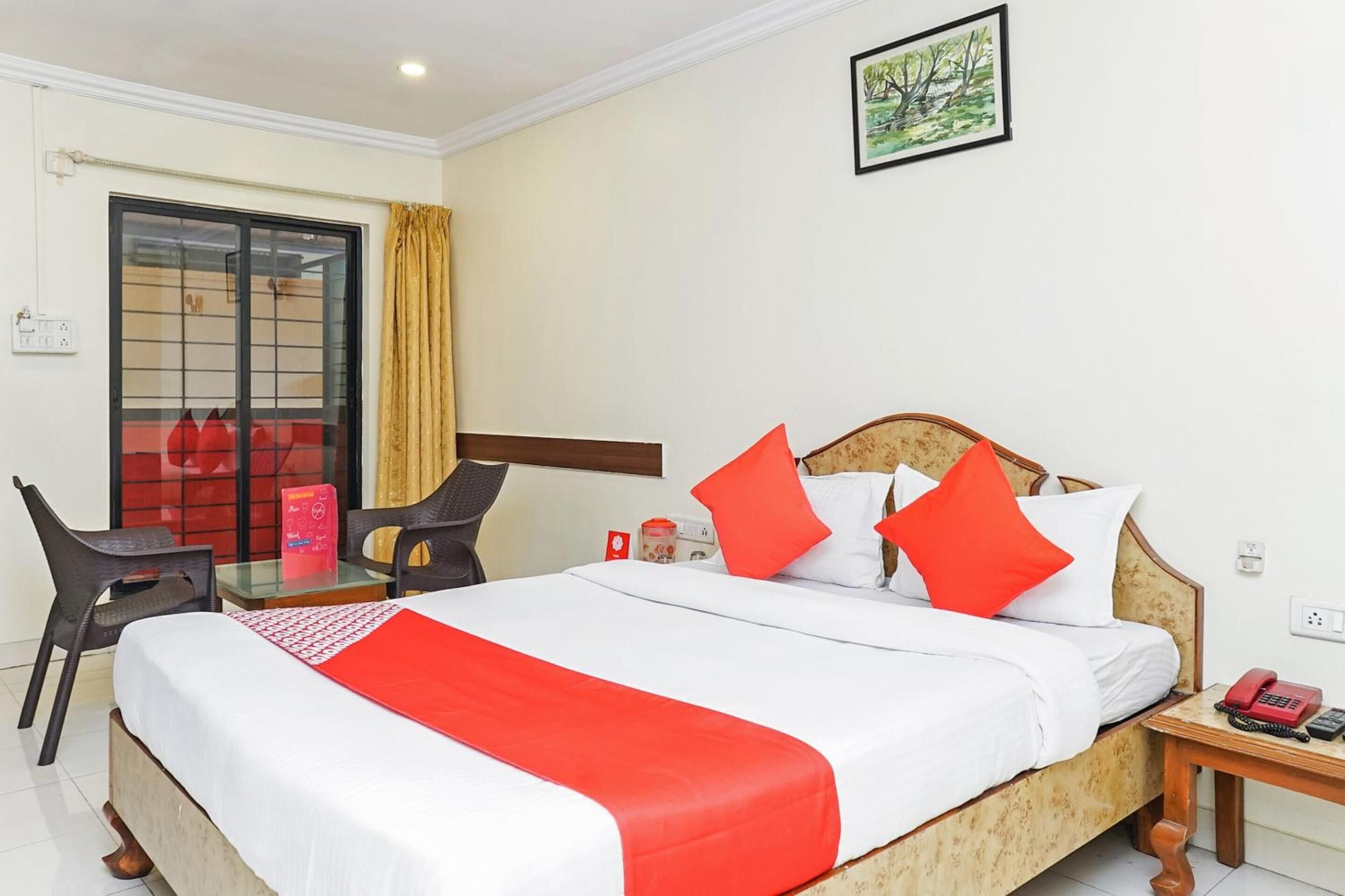 A hotel room with a bed, a desk, a chair, a telephone, and a window with curtains.