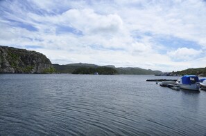 A calm lake with boats docked on the right, surrounded by rocky cliffs and distant hills.