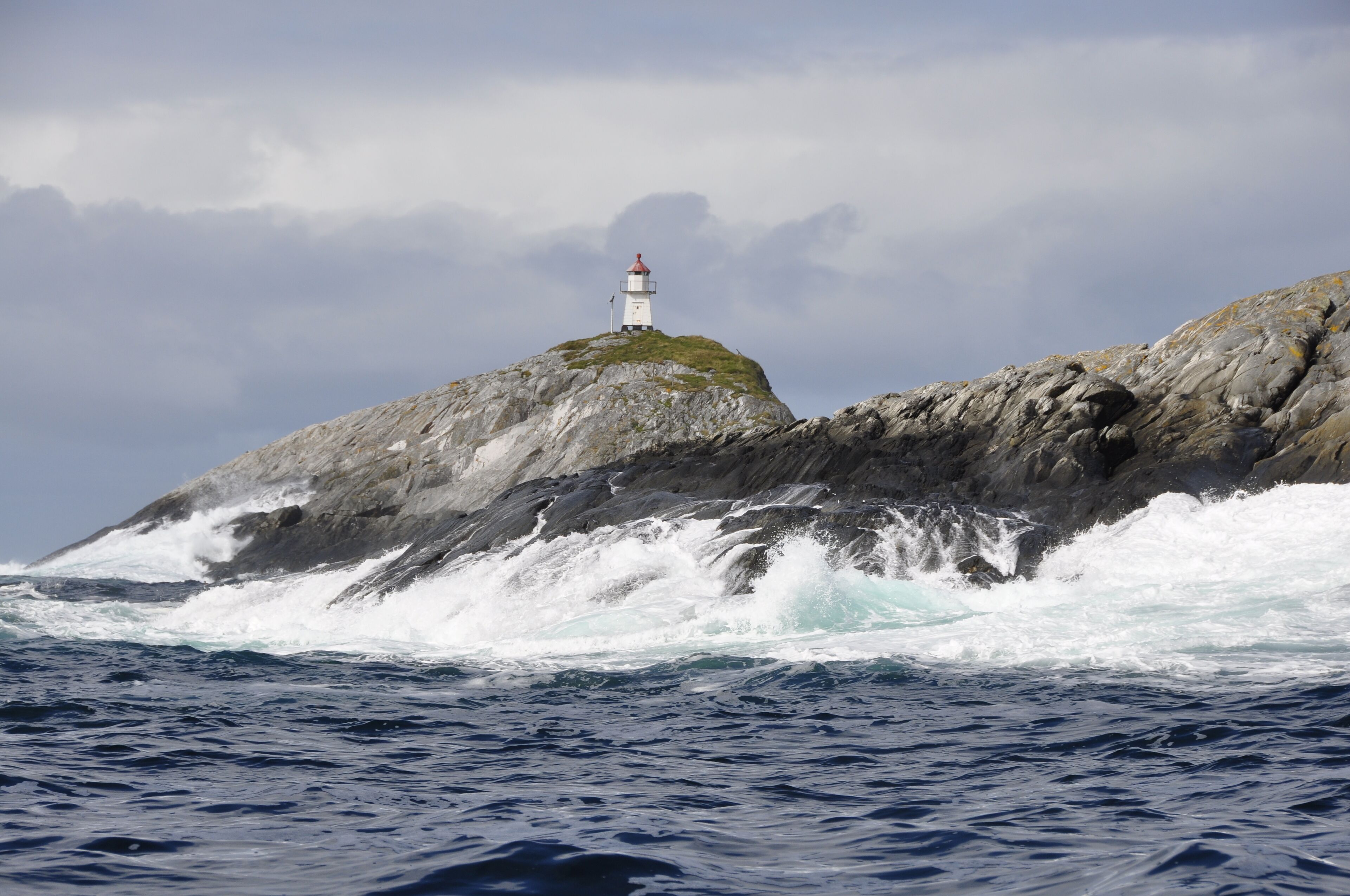 A lighthouse on a rocky outcrop with waves crashing against it.
