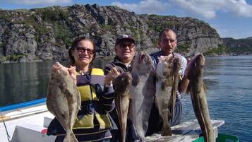 Three people holding fish on a boat with a rocky shoreline in the background.