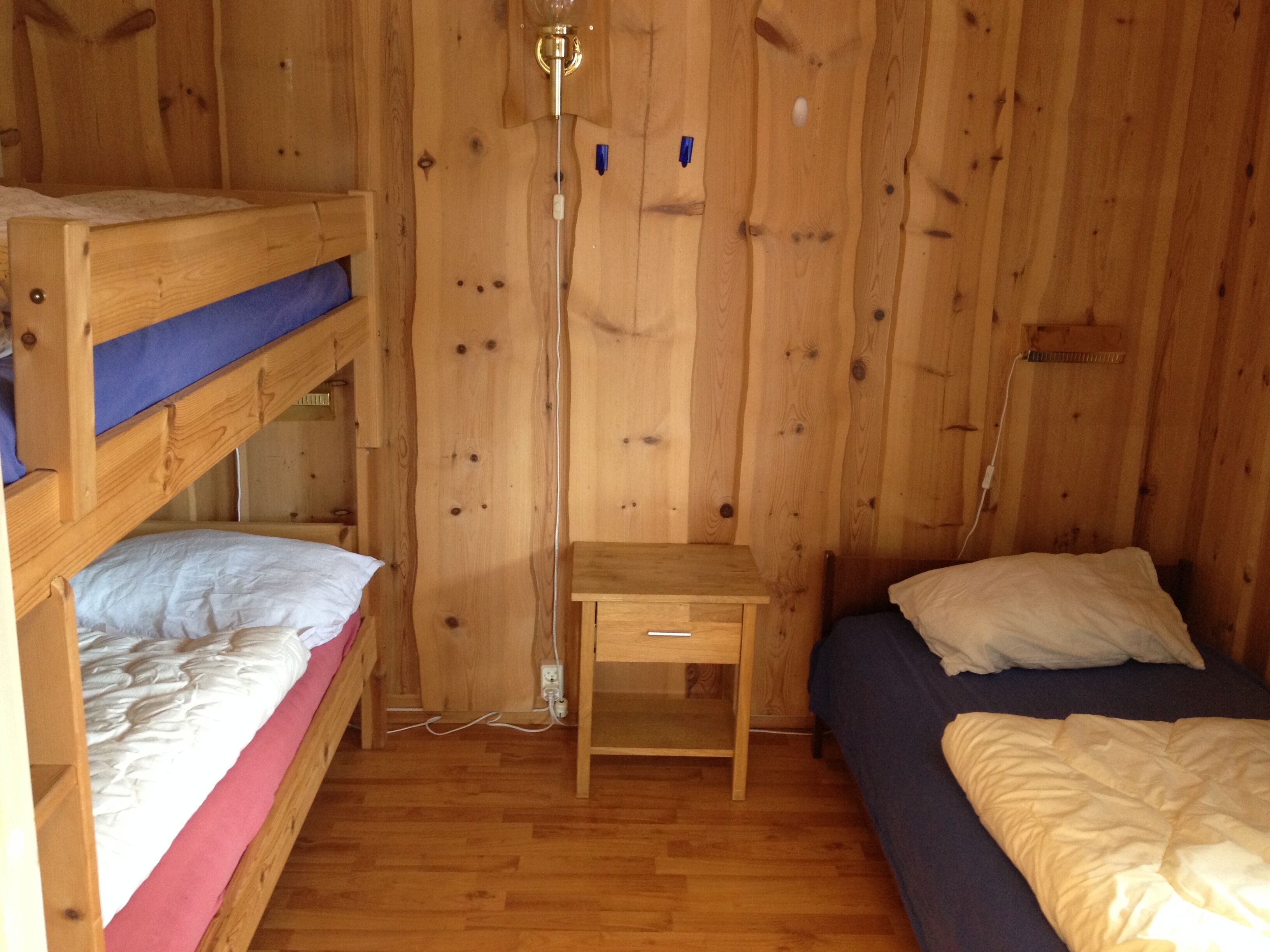 A wooden room with bunk beds, a small wooden table, and a wall-mounted lamp.