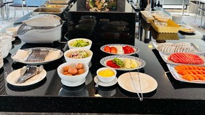 A buffet setup with various food items, a decorative floral arrangement, and a television screen in the background. - Pratunam Atrium Hotel (Bangkok)