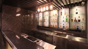 A modern bar area with a polished granite countertop, stainless steel appliances, and a variety of liquor bottles displayed on glass shelves. - Pratunam Atrium Hotel (Bangkok)