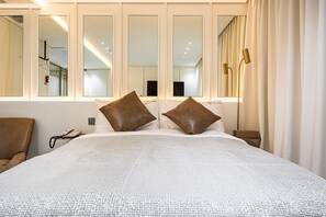 Une chambre d’hôtel avec un grand lit, deux oreillers marron, une table de chevet avec une lampe et une chaise.