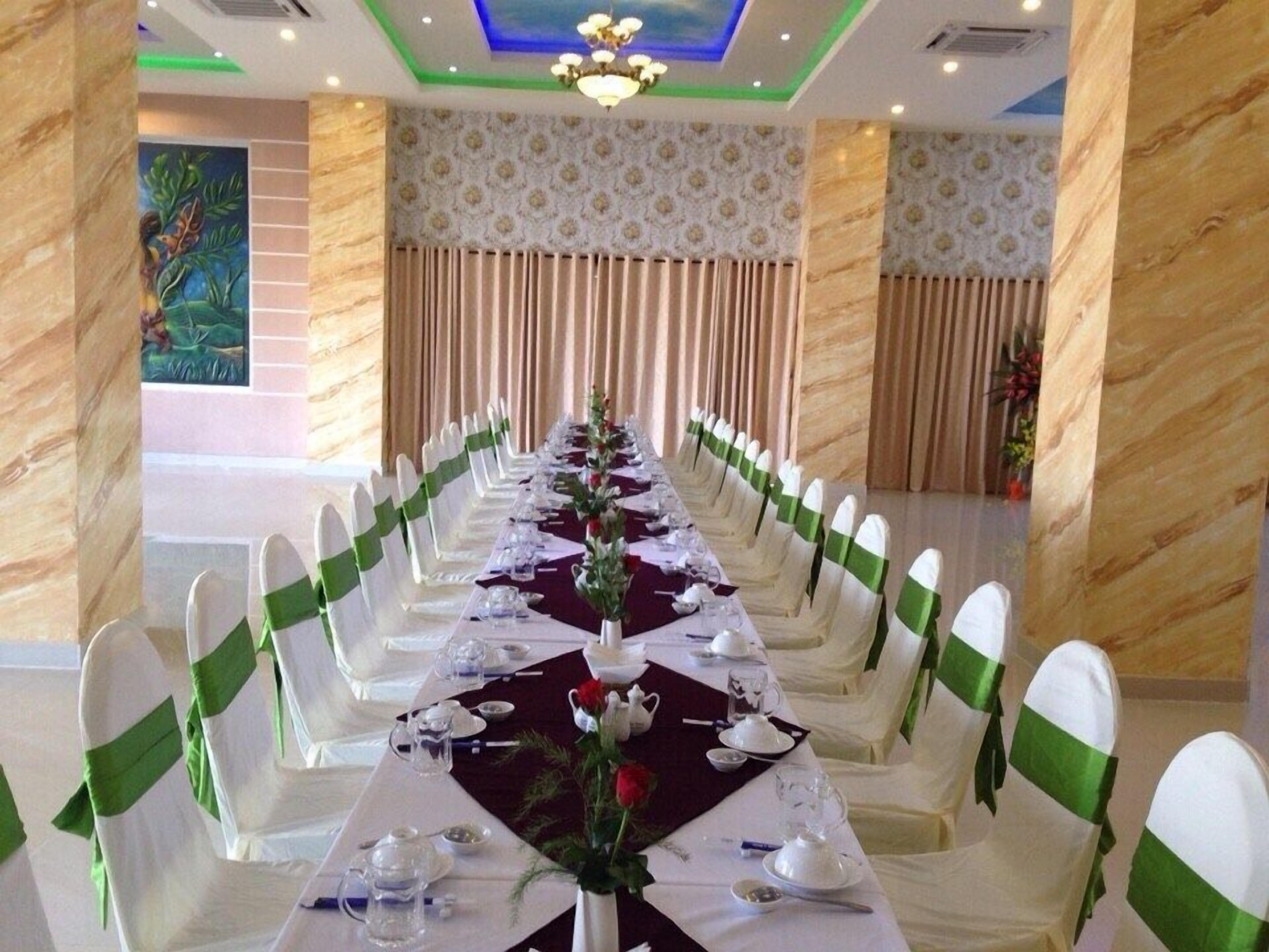 A long banquet table with white chairs, green sashes, and a dark tablecloth.